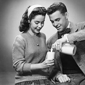 Young couple pouring milk from bottle to glass in studio, (B&W)