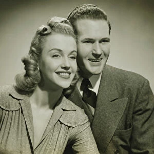 Young couple smiling in studio, (B&W), close-up