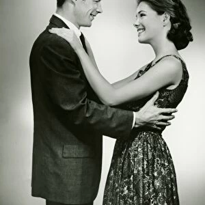Young couple standing face to face, smiling, in studio, (B&W)