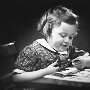 Young girl (4-5) at table cutting paper with scissors, (B&W), close-up