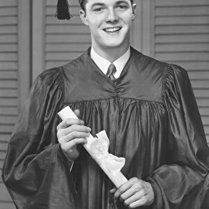 Young male university graduate holding diploma, (B&W), portrait