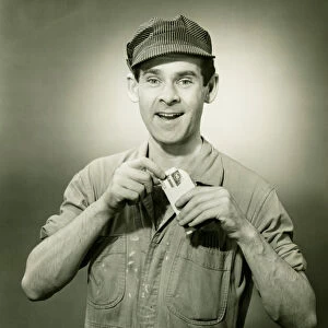 Young man in overalls showing card in studio, (B&W), portrait