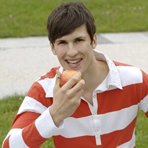 Young man sitting on a lawn eating an apple