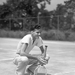 Young Man Smiling Squatting Holds Tennis Racquet A