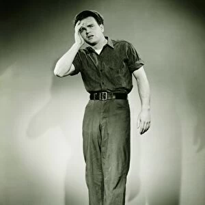 Young man standing in studio, holding hand on forehead, (B&W)