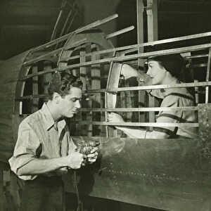 Young man and woman working in plane body in factory, (B&W)