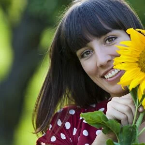 Young woman, 25, holding a sunflower in front of her face