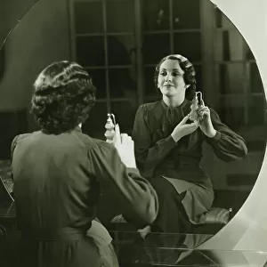Young woman applying perfume in front of mirror, (B&W)