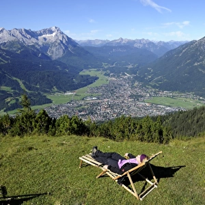 Young woman in a deck chair, view of Garmisch-Partenkirchen, Zugspitze mountain, Jubilaeumsgrat ridge and Alpspitze mountain as seen from Wank mountain, Upper Bavaria, Bavaria, Germany, Europe