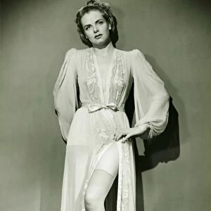 Young woman in dressing gown standing in studio, showing off leg, (B&W)