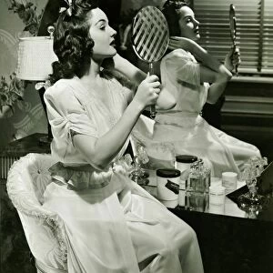 Young woman examining make-up in mirror, (B&W)