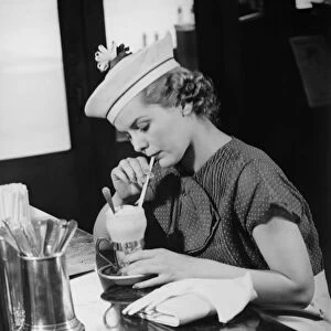 Young woman in fancy hat drinking ice cream soda (B&W)