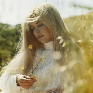 Young woman in field holding flower, eyes closed