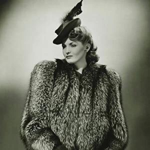 Young woman in fur coat and fashionable hat in studio, (B&W)