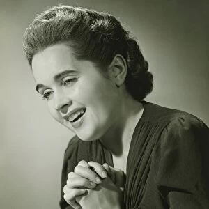 Young woman with hands put together smiling in studio (B&W), close-up