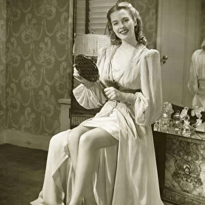Young woman holding mirror, sitting at dresser, (B&W)