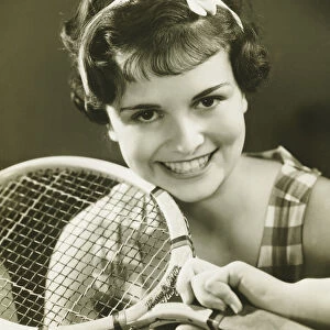 Young woman holding tennis racket, smiling, (B&W), portrait