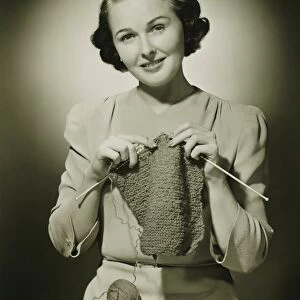 Young woman knitting in studio, (B&W), portrait