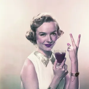 Young woman showing v sign with wine glass, smiling, portrait