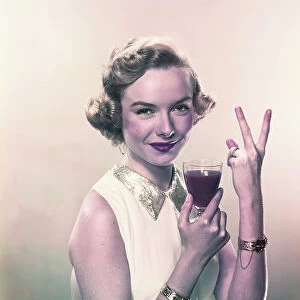 Young woman showing v sign with wine glass, smiling, portrait