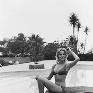 Young woman sitting on sun lounger by swimming pool, smiling, portrait