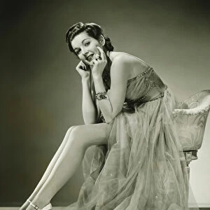 Young woman wearing evening dress, sitting in studio, (B&W)
