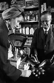 Prints of 20th December 1941: A woman buying onions in a small shop rejects one that is sprouting when shopping during WW II Discover the Vision of Haywood Magee – A Master of Mid-Century British Life: Not That One
