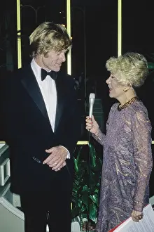 Prints of American actor Robert Redford, wearing a tuxedo and a bow tie, is interviewed by American gossip columnist Rona Barrett, who wears a purple-and-gold paisley pattern dress and a thick gold necklace Robert Redford: Classic Hollywood Elegance: 53rd Academy Awards