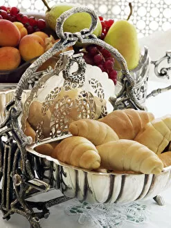 Opened Gallery: Antique silver hinged bread basket with croissants in front of a bowl of fruit on a breakfast table