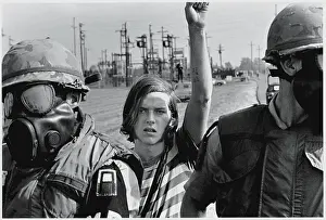 Prints of A young man raises his arm in protest behind a line of American soldiers from the First Army who wear gas masks and flak jackets during an antiwar protest at Fort Dix, New Jesrey, October 12, 1969 Vietnam War Prints: Antiwar Protest At Ft. Dix