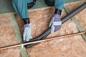 Images Dated 7th July 2004: Attaching pipe insulation to a copper pipe above joists and insulation blanket