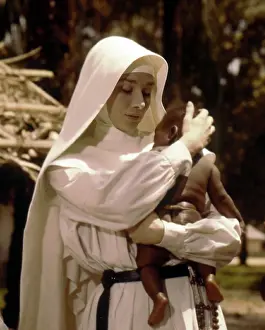 Prints of Actress Audrey Hepburn holds a baby in a scene of the film 'The Nun's Story' at Congo, in 1958. (Photo by Leo Fuchs/Getty Images) Elegance Personified – A Classic Art Print Collection: Audrey Hepburn With Baby