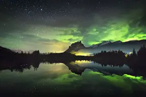 The aurora reflected in a small lake below Castle Mountain as a train light goes by, Banff National Park, Alberta, Canada