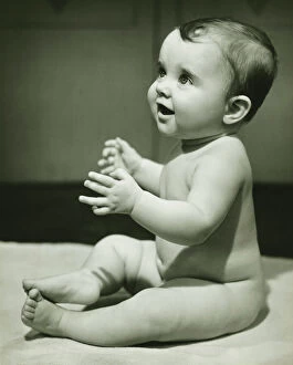 Baby boy (12-18 months) with raised hands, sitting on bedspread, (B&W), close-up