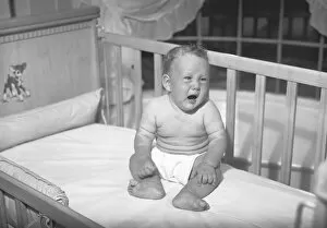 Baby boy (6-9 months) sitting in crib, crying, (B&W)