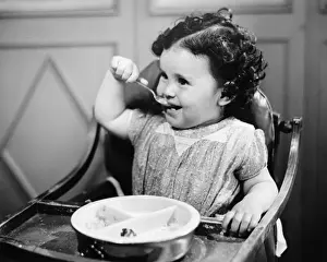 12 17 Months Prints: Baby girl (12-18 months) in highchair eating, (B&W)