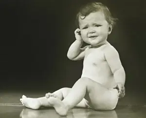 Baby girl (9-12 months) sitting on floor in studio, (B&W)
