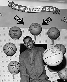 Prints of 1960: American basketball player Wilt Chamberlain wearing a business suit, smiling and seated at the Spalding basketball display at the opening of a Sporting Goods Fair, Hotel New Yorker Courtside Vibes: Stunning Basketball Prints: Balls Around