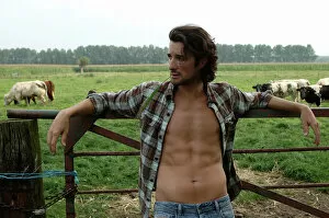 Clothing Gallery: Bare-chested cowboy leaning on a cow gate