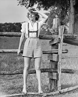 Blonde Hair Prints: Barefoot woman in shorts standing on wooden fence on meadow, (B&W)