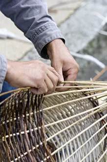 A basket weaver sitting on the street and weaving a basket, Brittany, France, Europe