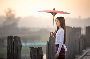 Beautiful woman holding traditional red umbrella and walking on U Bein Bridge, Myanmar
