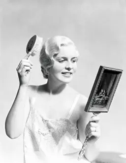 One Mid Adult Woman Only Prints: Beautiful woman wearing slip, looking in mirror and brushing hair