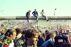Prints of Three people sit on top of the graffiti-covered Berlin Wall with a crowd below them on November 12, 1989 in Berlin, Germany. (Photo by Roxanne McCann/Getty Images.) Timeless Moments: A Visual Journey Through History’s Defining Images: Berlin Wall Pepsi Commercial