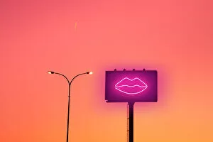Billboard with sexy lips neon light and sunset sky in the city