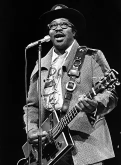 Prints of circa 1970: American rock guitarist and singer Bo Diddley stands and sings at a microphone, playing his rectangular-shaped electric guitar during a concert performance Bo Diddley: Rhythm & Riffs Prints: Bo Diddley