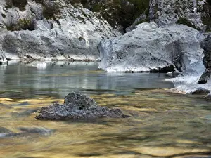 Flowing Prints: Boulders and rocks in the river bed of the golden coloured Soca river in Soca Valley near Bovec