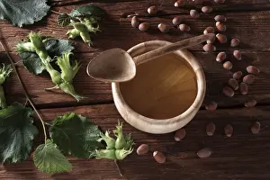 Spoon Prints: A bowl of hazelnut oil and some ripe and unripe hazelnuts (Corylus avellana) on rustic wooden boards
