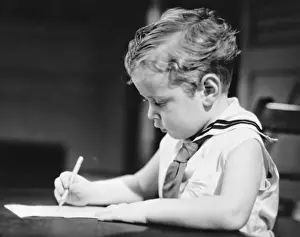 Focused Prints: Boy (4-5) wearing sailor suit drawing at table, (B&W)