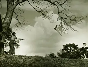 Boy (6-7) flying kite in park, (B&W)